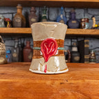 Front view of a handmade Scroll Mug designed to look like an old rolled parchment with a sandy base, a brown ribbon, a greenish-blue cord and a red wax seal featuring a vampire emblem.