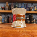 Three-quarter right side view of a handmade Scroll Mug designed to look like an old rolled parchment with a sandy base, a brown ribbon, a greenish-blue cord and a red wax seal featuring a vampire emblem.