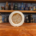 Bottom view of a handmade Scroll Mug with the Handy Goblin logo embossed in the centre, featuring a beige base.