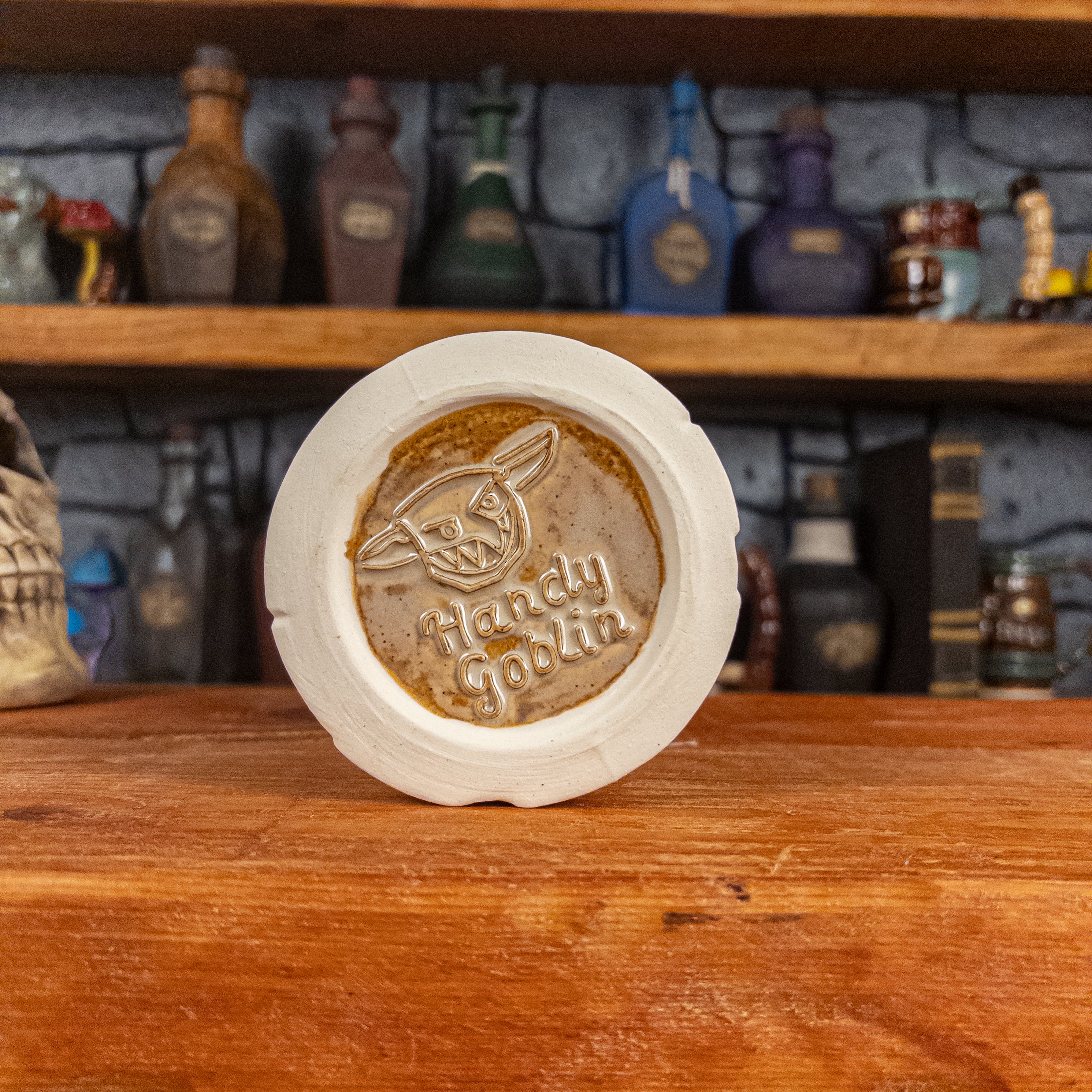 Bottom view of a handmade Scroll Mug with the Handy Goblin logo embossed in the centre, featuring a beige base.