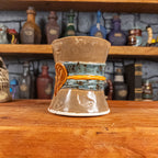 Three-quarter right side view of a handmade Scroll Mug designed to look like an old rolled parchment with a brown base, a speckled blue ribbon, an orange cord and a brown wax seal featuring a vampire emblem.