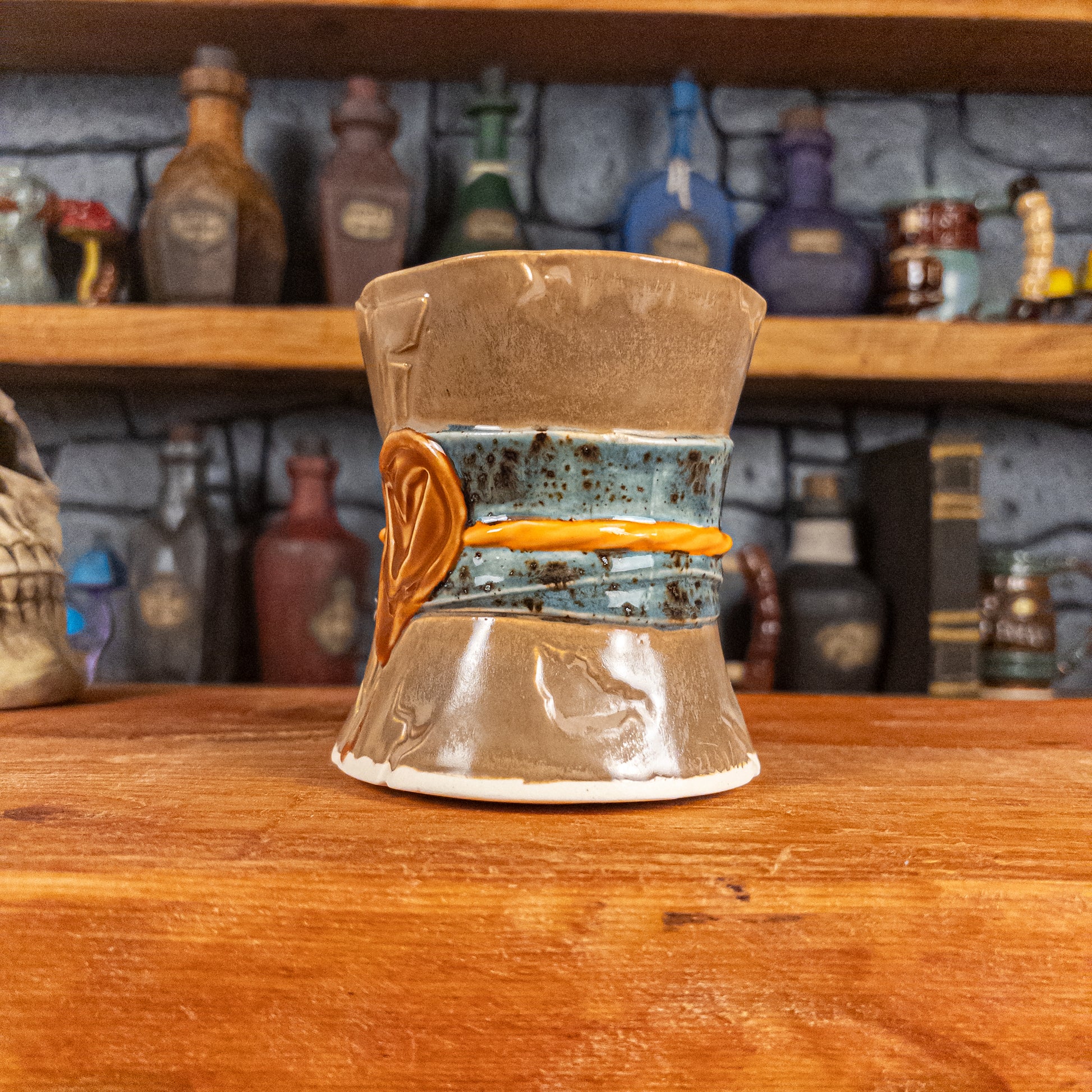 Three-quarter right side view of a handmade Scroll Mug designed to look like an old rolled parchment with a brown base, a speckled blue ribbon, an orange cord and a brown wax seal featuring a vampire emblem.