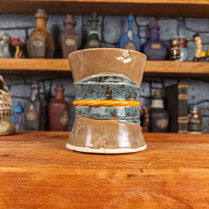 Back view of a handmade Scroll Mug designed to look like an old rolled parchment with a brown base, a speckled blue ribbon and an orange cord.