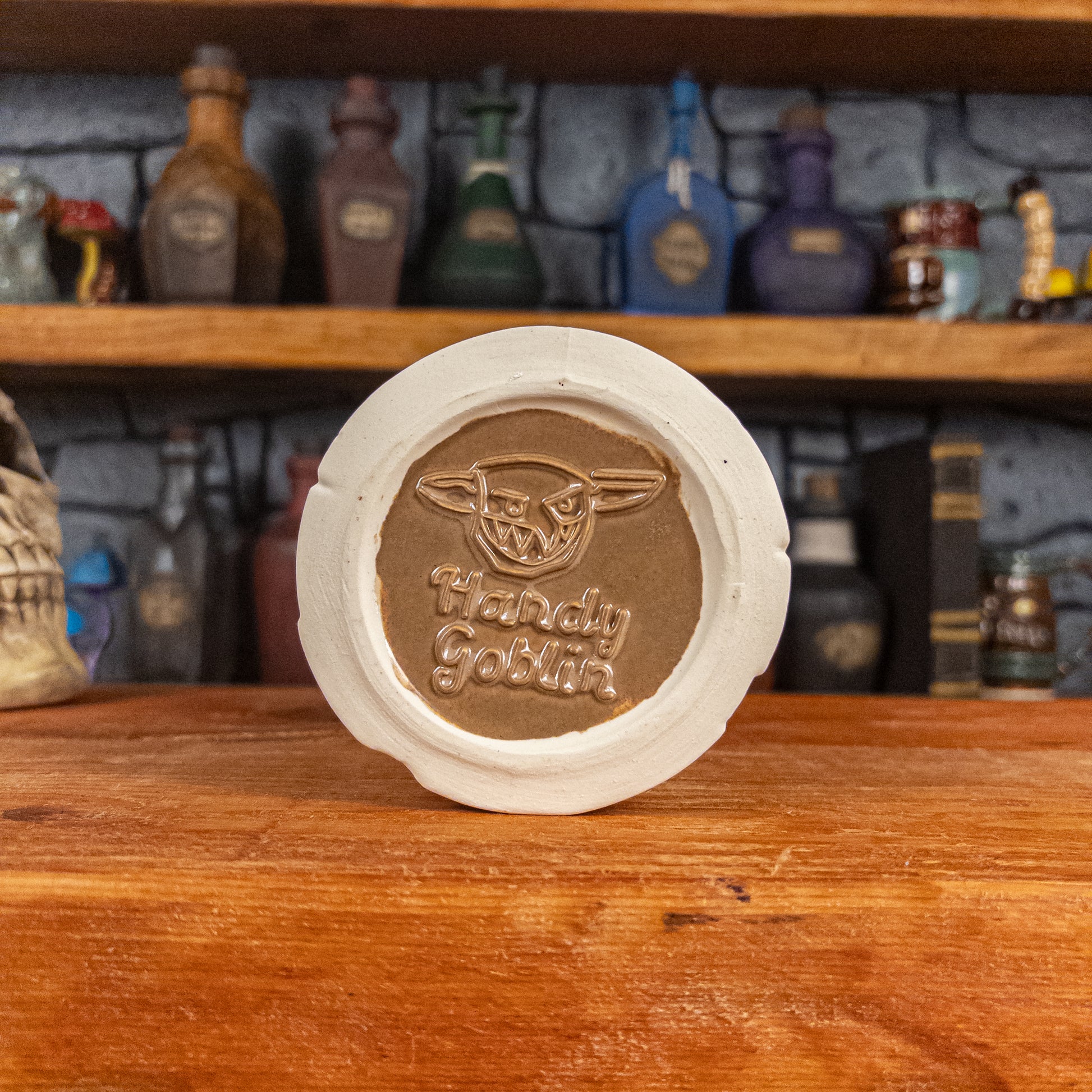 Bottom view of a handmade Scroll Mug with the Handy Goblin logo embossed in the centre, featuring a brown base.