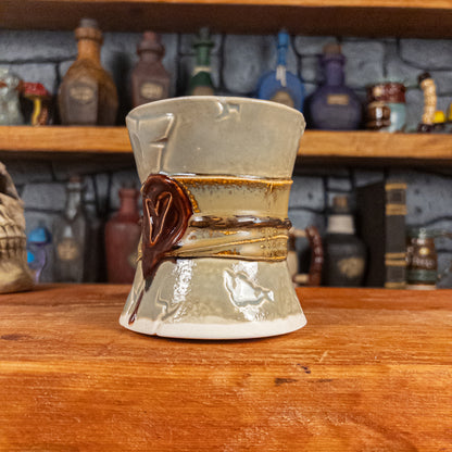 Three-quarter right side view of a handmade Scroll Mug designed to look like an old rolled parchment with a light grey base, a light brown ribbon, a dark brown cord and a dark red wax seal featuring a vampire emblem.