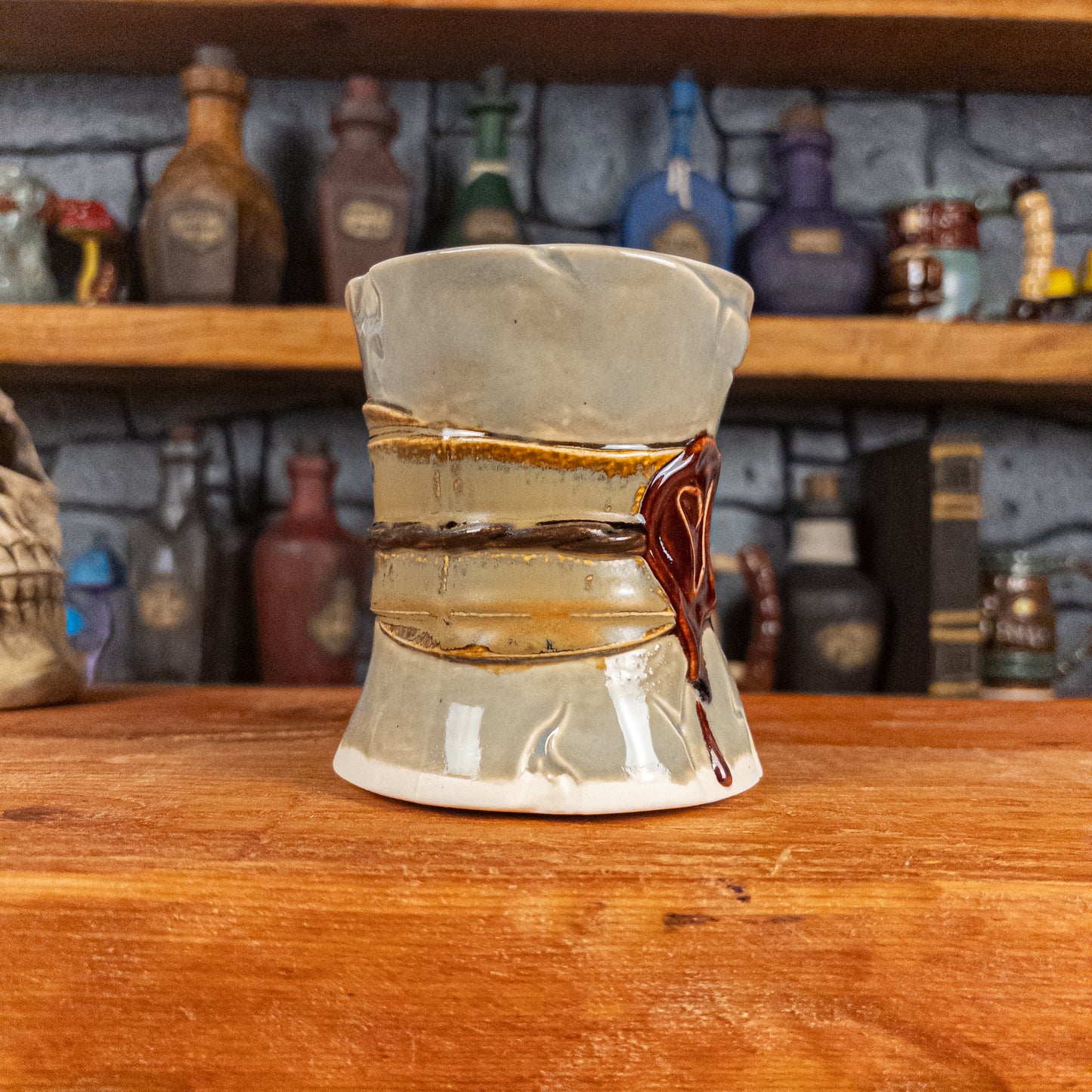 Three-quarter left side view of a handmade Scroll Mug designed to look like an old rolled parchment with a light grey base, a light brown ribbon, a dark brown cord and a dark red wax seal featuring a vampire emblem.