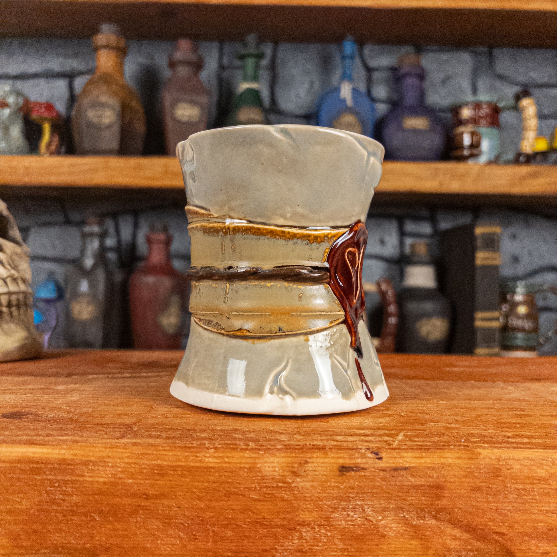 Three-quarter left side view of a handmade Scroll Mug designed to look like an old rolled parchment with a light grey base, a light brown ribbon, a dark brown cord and a dark red wax seal featuring a vampire emblem.