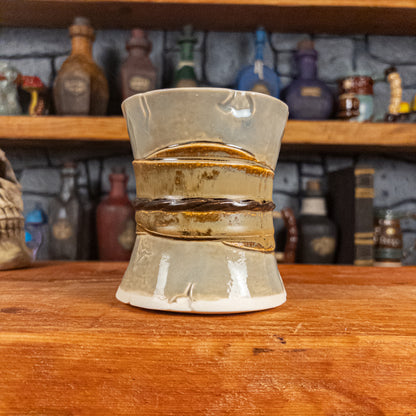 Back view of a handmade Scroll Mug designed to look like an old rolled parchment with a light grey base, a light brown ribbon and a dark brown cord.