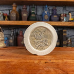 Bottom view of a handmade Scroll Mug with the Handy Goblin logo embossed in the centre, featuring a speckled light grey base.