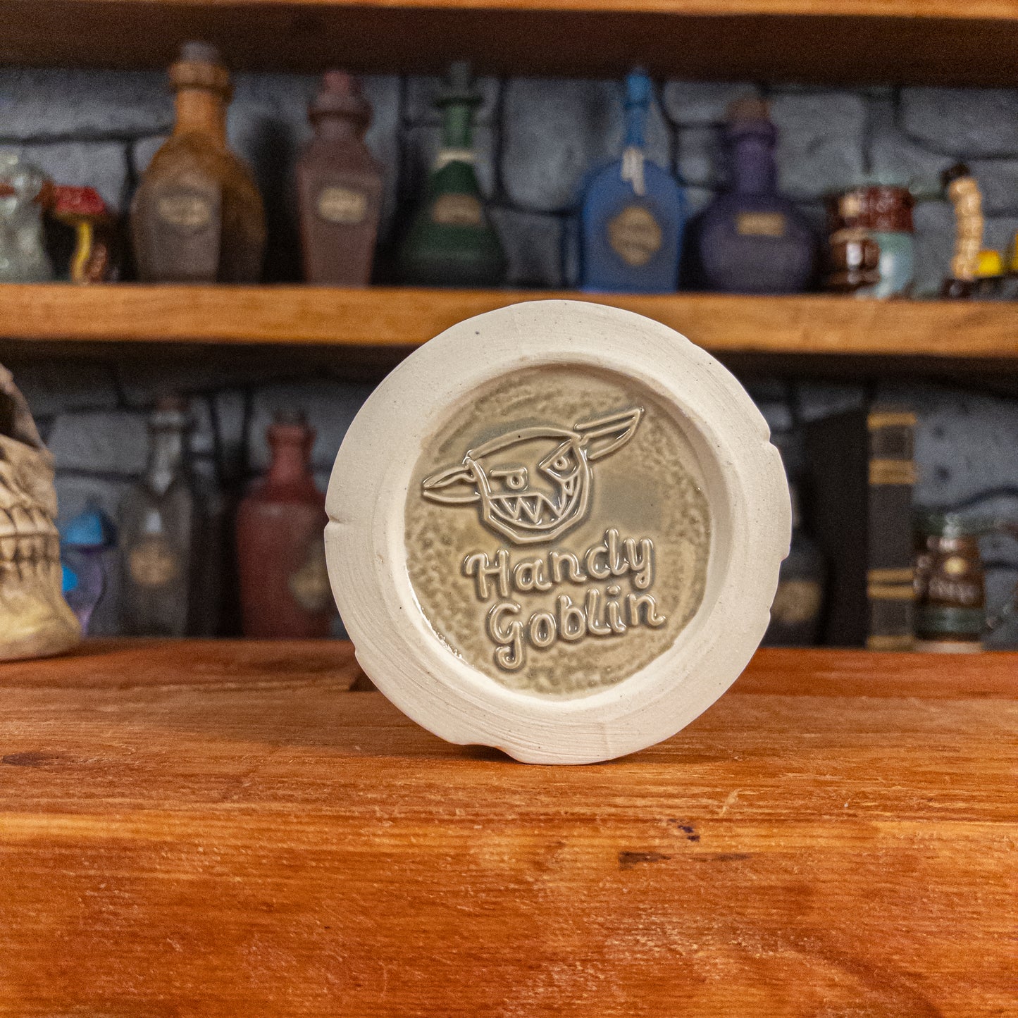 Bottom view of a handmade Scroll Mug with the Handy Goblin logo embossed in the centre, featuring a speckled light grey base.