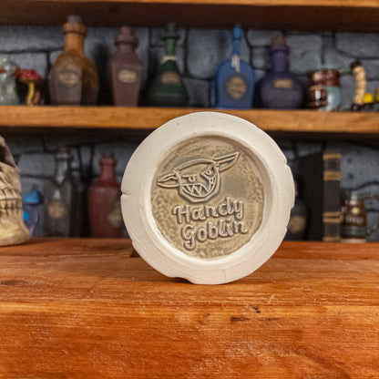 Bottom view of a handmade Scroll Mug with the Handy Goblin logo embossed in the centre, featuring a speckled light grey base.