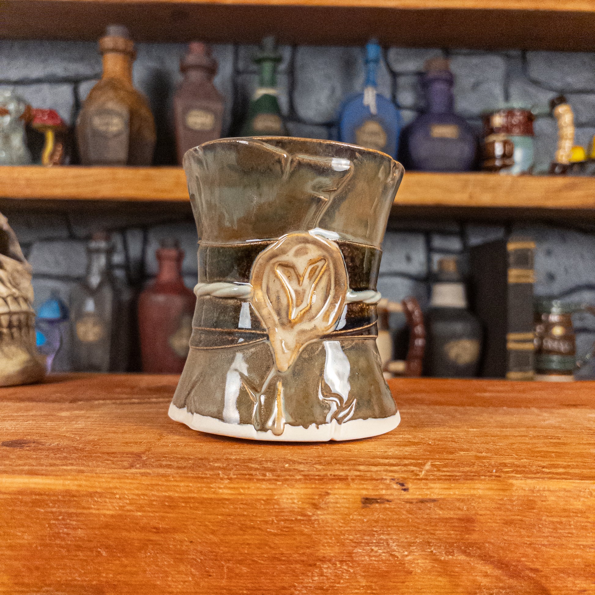 Front view of a handmade Scroll Mug designed to look like an old rolled parchment with a brown base, a brown-green ribbon, a light green cord and a beige wax seal featuring a vampire emblem.