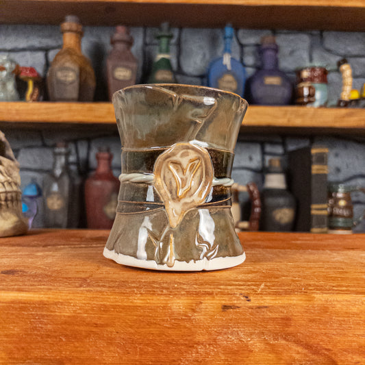 Front view of a handmade Scroll Mug designed to look like an old rolled parchment with a brown base, a brown-green ribbon, a light green cord and a beige wax seal featuring a vampire emblem.