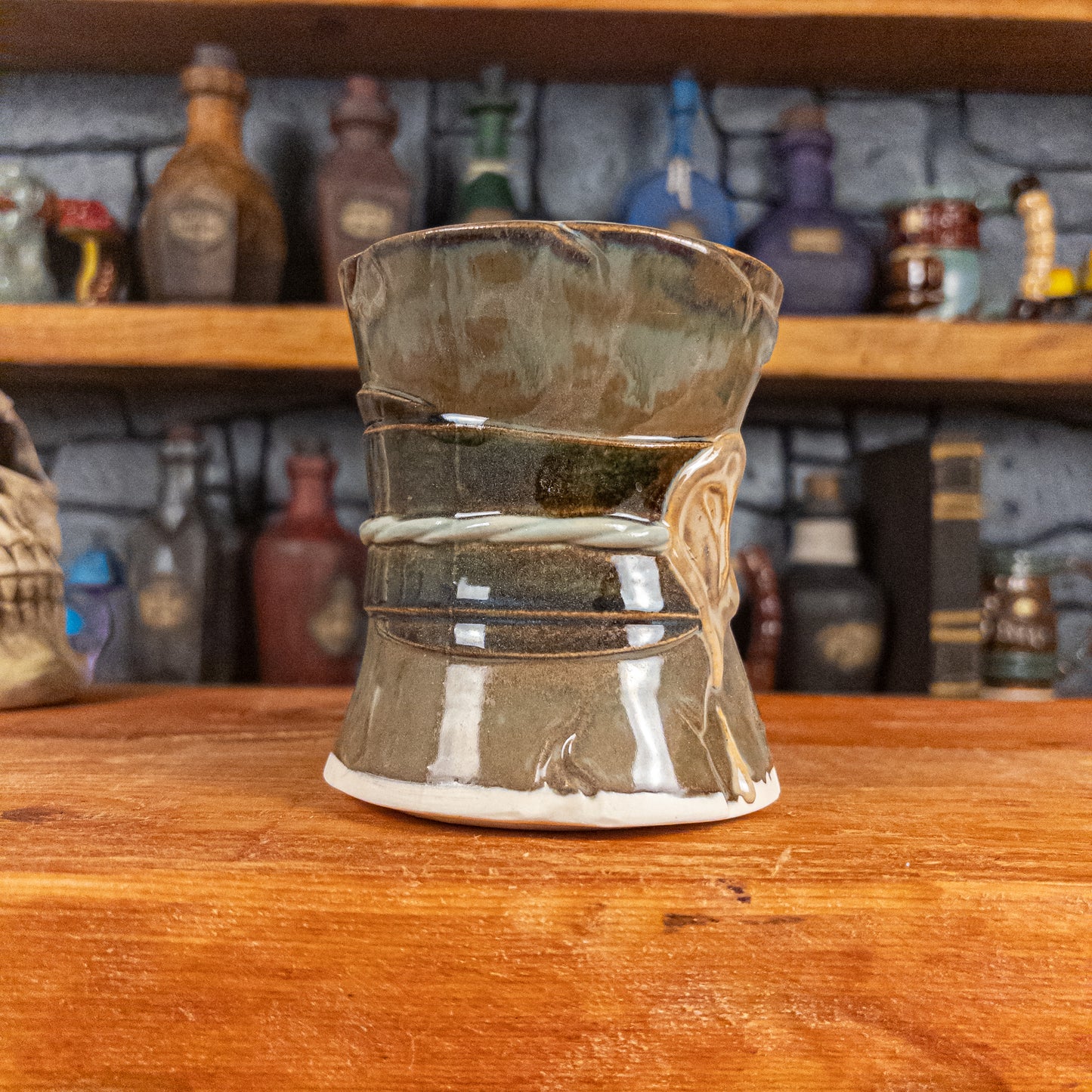 Three-quarter left side view of a handmade Scroll Mug designed to look like an old rolled parchment with a brown base, a brown-green ribbon, a light green cord and a beige wax seal featuring a vampire emblem.