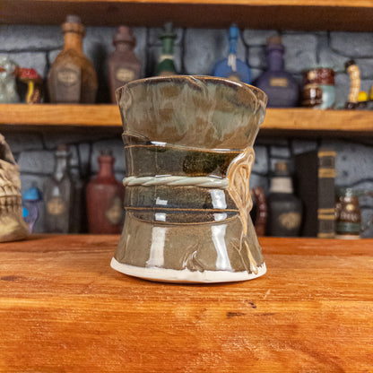 Three-quarter left side view of a handmade Scroll Mug designed to look like an old rolled parchment with a brown base, a brown-green ribbon, a light green cord and a beige wax seal featuring a vampire emblem.