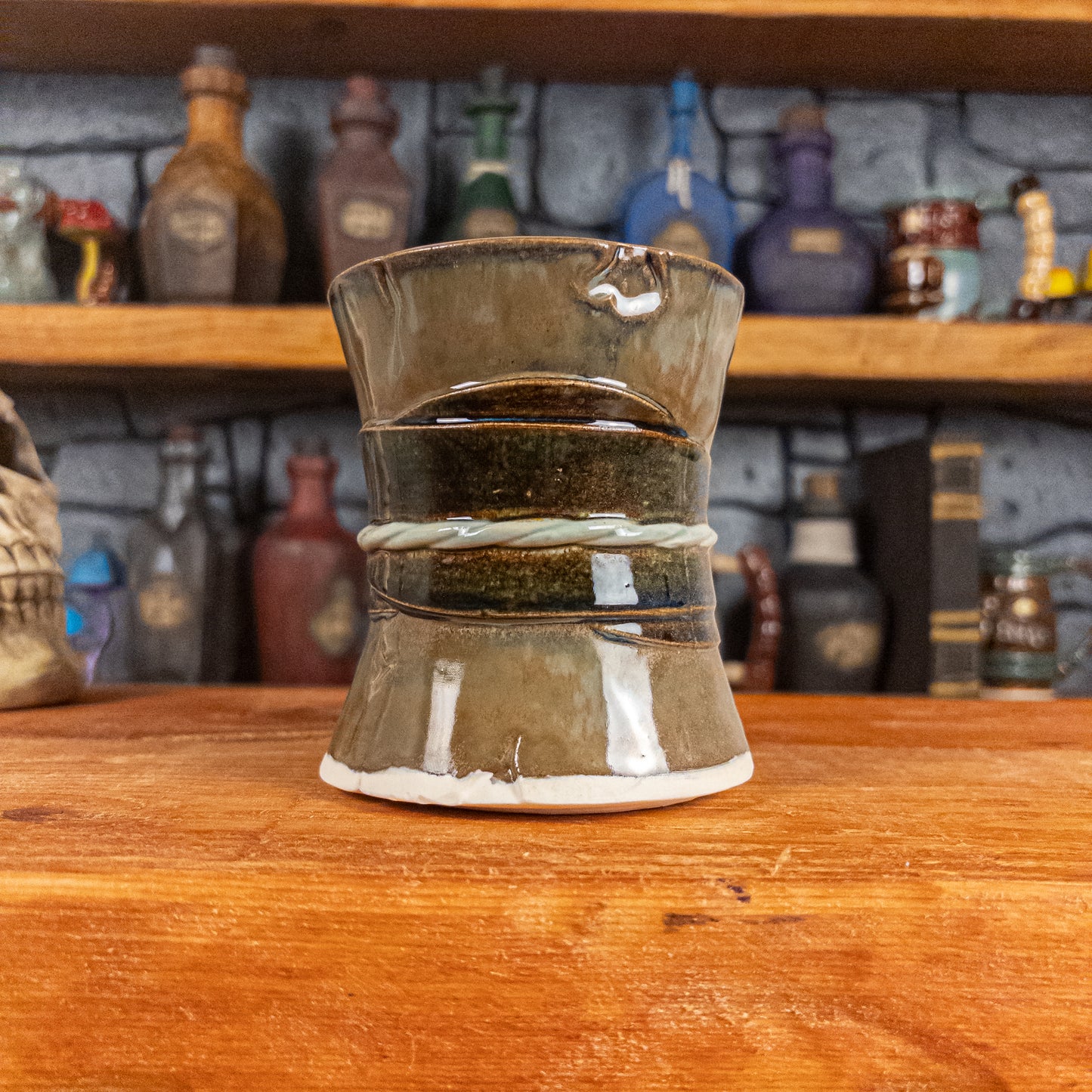 Back view of a handmade Scroll Mug designed to look like an old rolled parchment with a brown base, a brown-green ribbon and a light green cord.