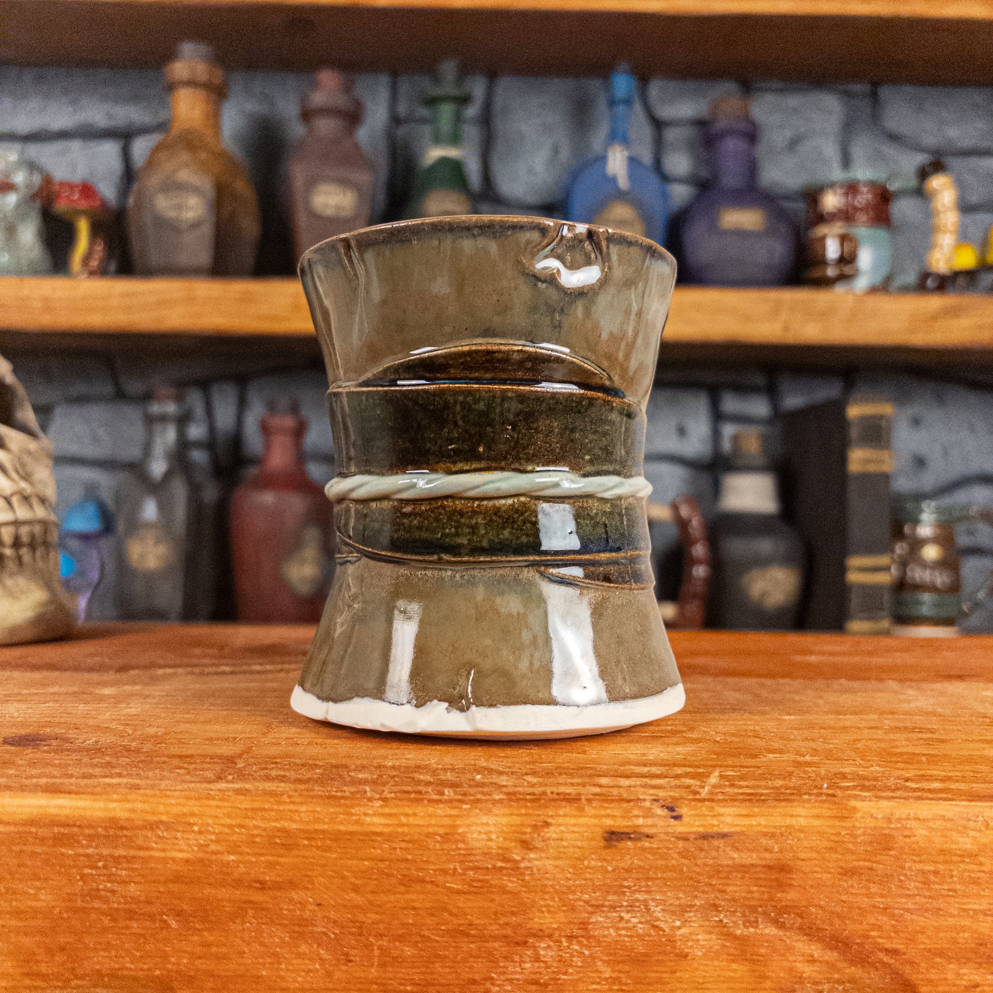 Back view of a handmade Scroll Mug designed to look like an old rolled parchment with a brown base, a brown-green ribbon and a light green cord.