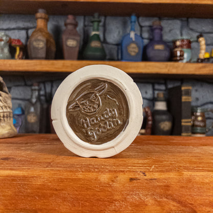 Bottom view of a handmade Scroll Mug with the Handy Goblin logo embossed in the centre, featuring a brown base.