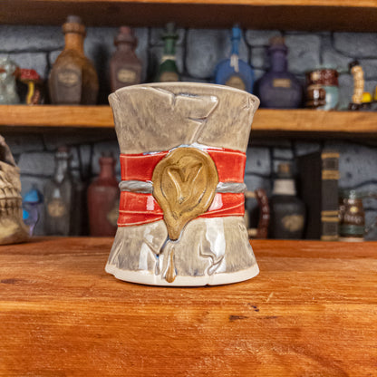 Front view of a handmade Scroll Mug designed to look like an old rolled parchment with a grey base, a red ribbon, a silver cord and a golden wax seal featuring a vampire emblem.