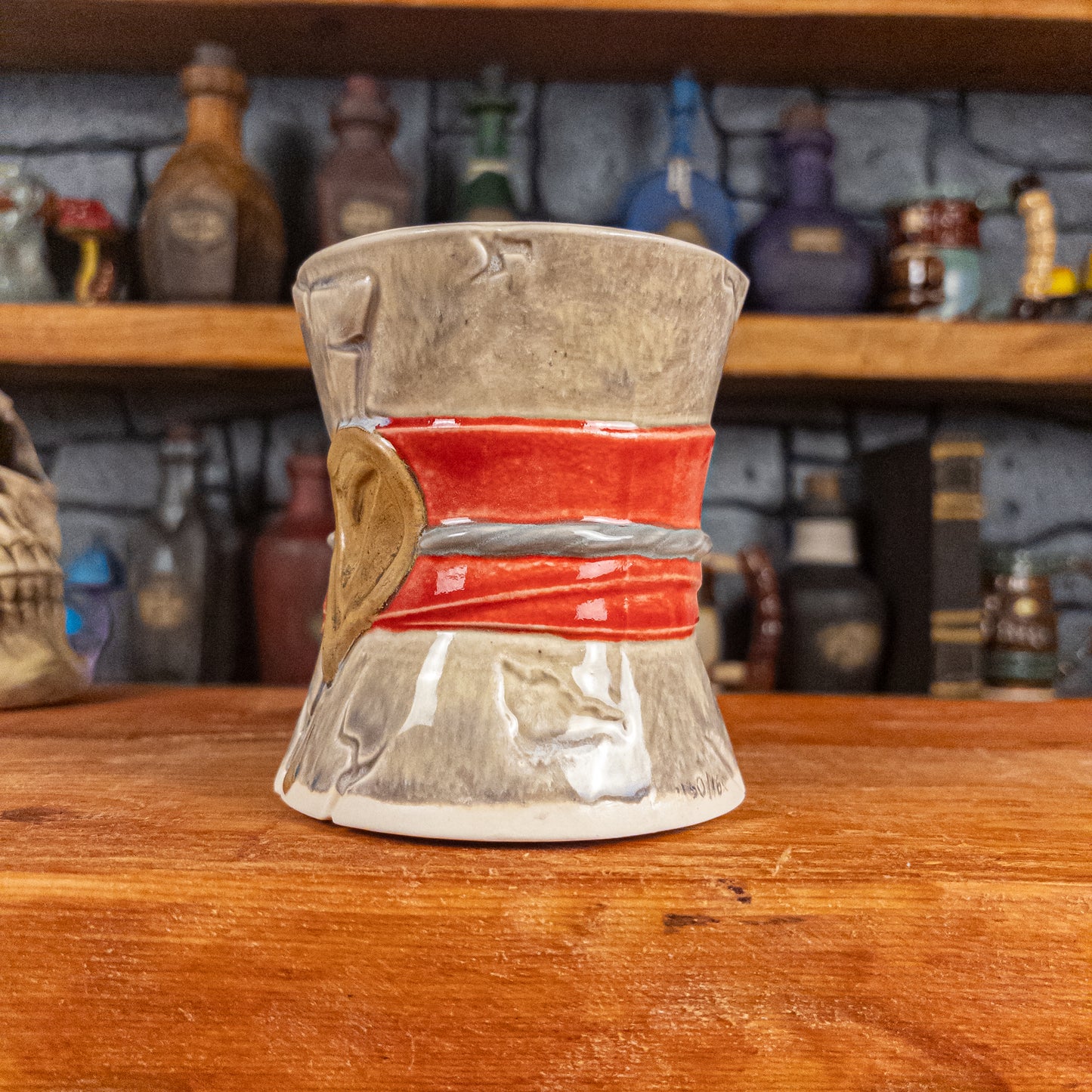 Three-quarter right side view of a handmade Scroll Mug designed to look like an old rolled parchment with a grey base, a red ribbon, a silver cord and a golden wax seal featuring a vampire emblem.