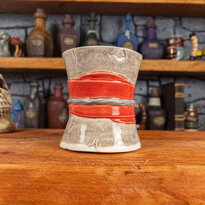 Back view of a handmade Scroll Mug designed to look like an old rolled parchment with a grey base, a red ribbon and a silver cord.
