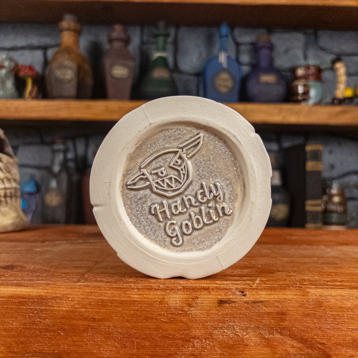 Bottom view of a handmade Scroll Mug with the Handy Goblin logo embossed in the centre, featuring a grey base.