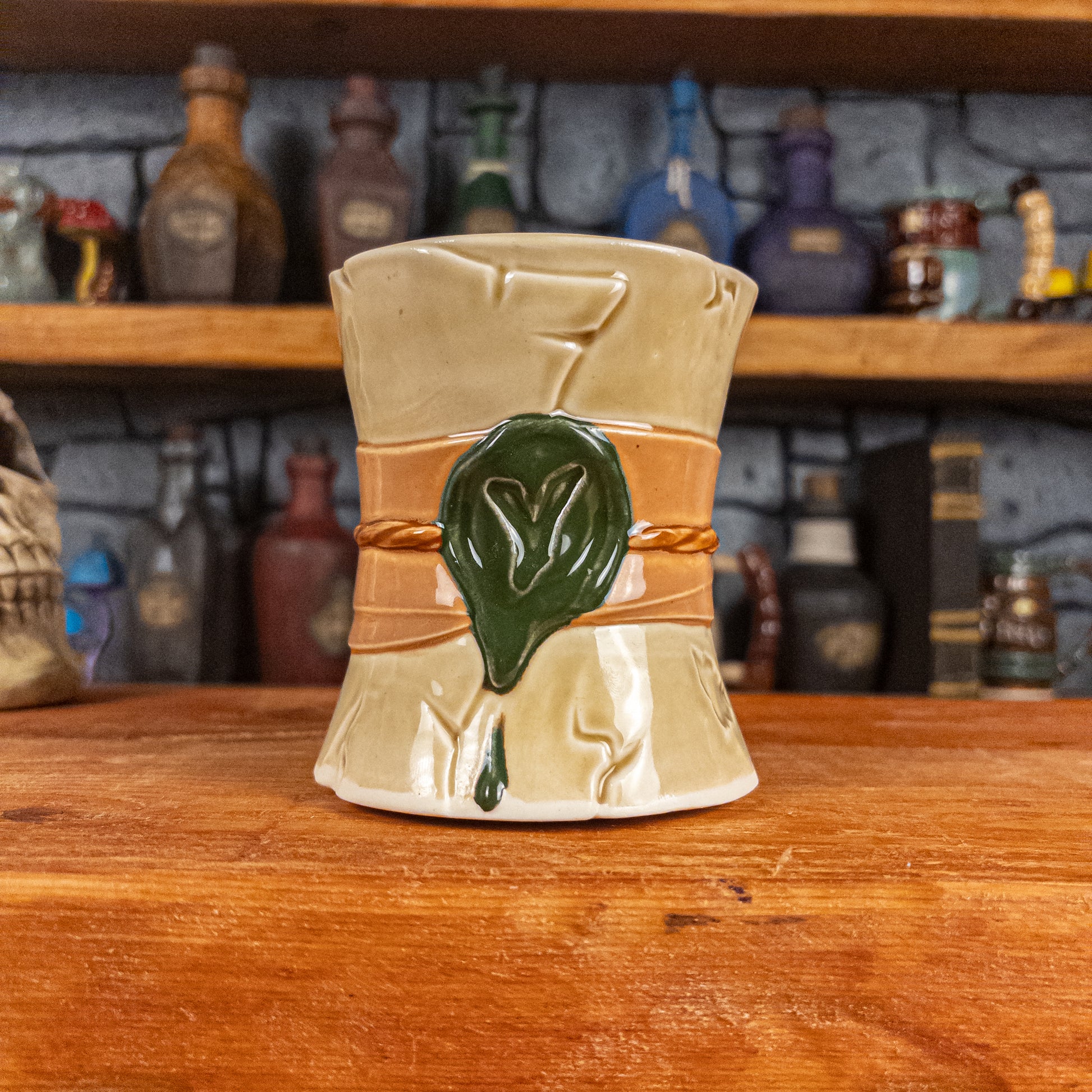 Front view of a handmade Scroll Mug designed to look like an old rolled parchment with a light-yellow base, a light orange ribbon, a light brown cord and a dark green wax seal featuring a vampire emblem.