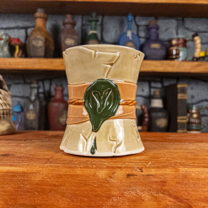 Front view of a handmade Scroll Mug designed to look like an old rolled parchment with a light-yellow base, a light orange ribbon, a light brown cord and a dark green wax seal featuring a vampire emblem.