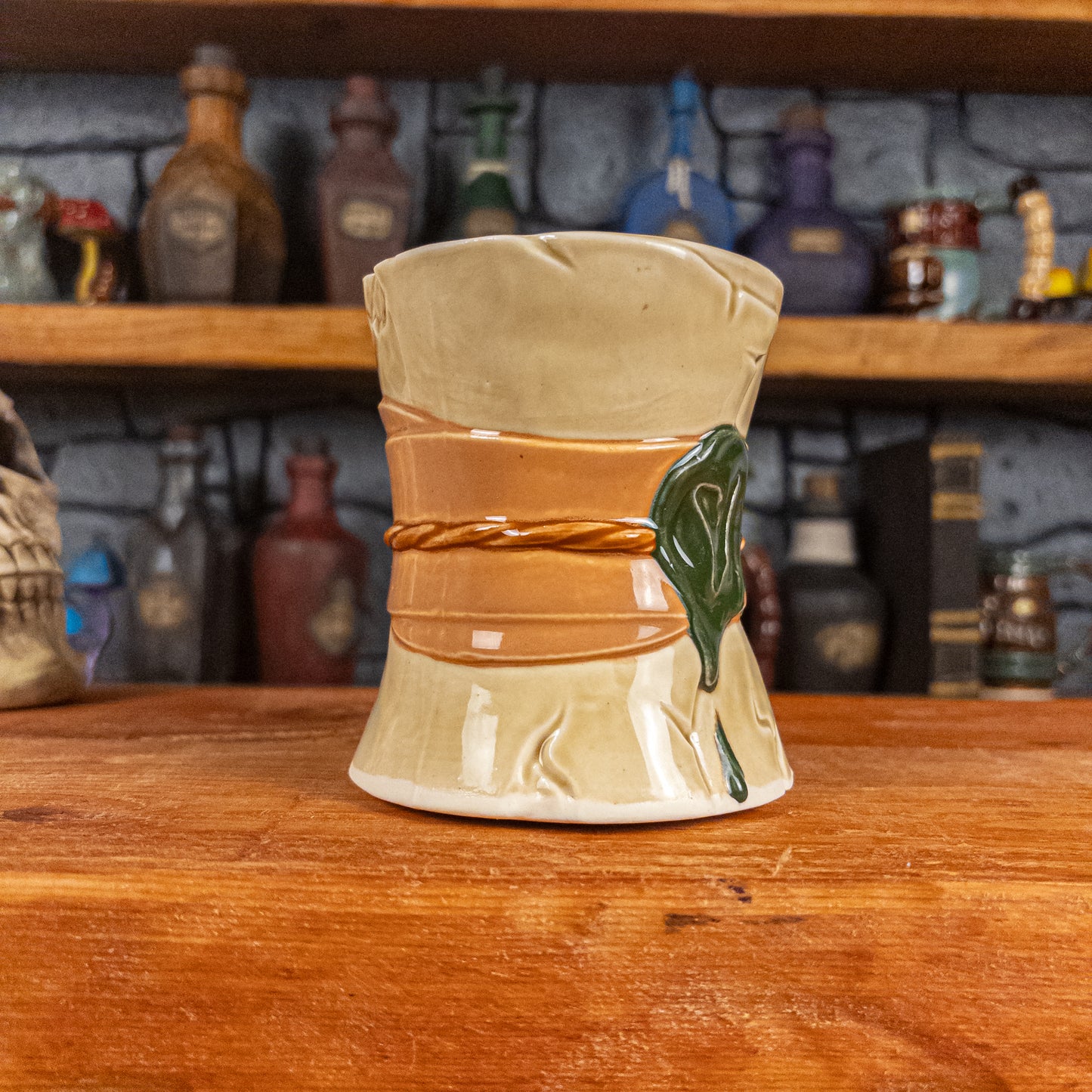 Three-quarter left side view of a handmade Scroll Mug designed to look like an old rolled parchment with a light-yellow base, a light orange ribbon, a light brown cord and a dark green wax seal featuring a vampire emblem.