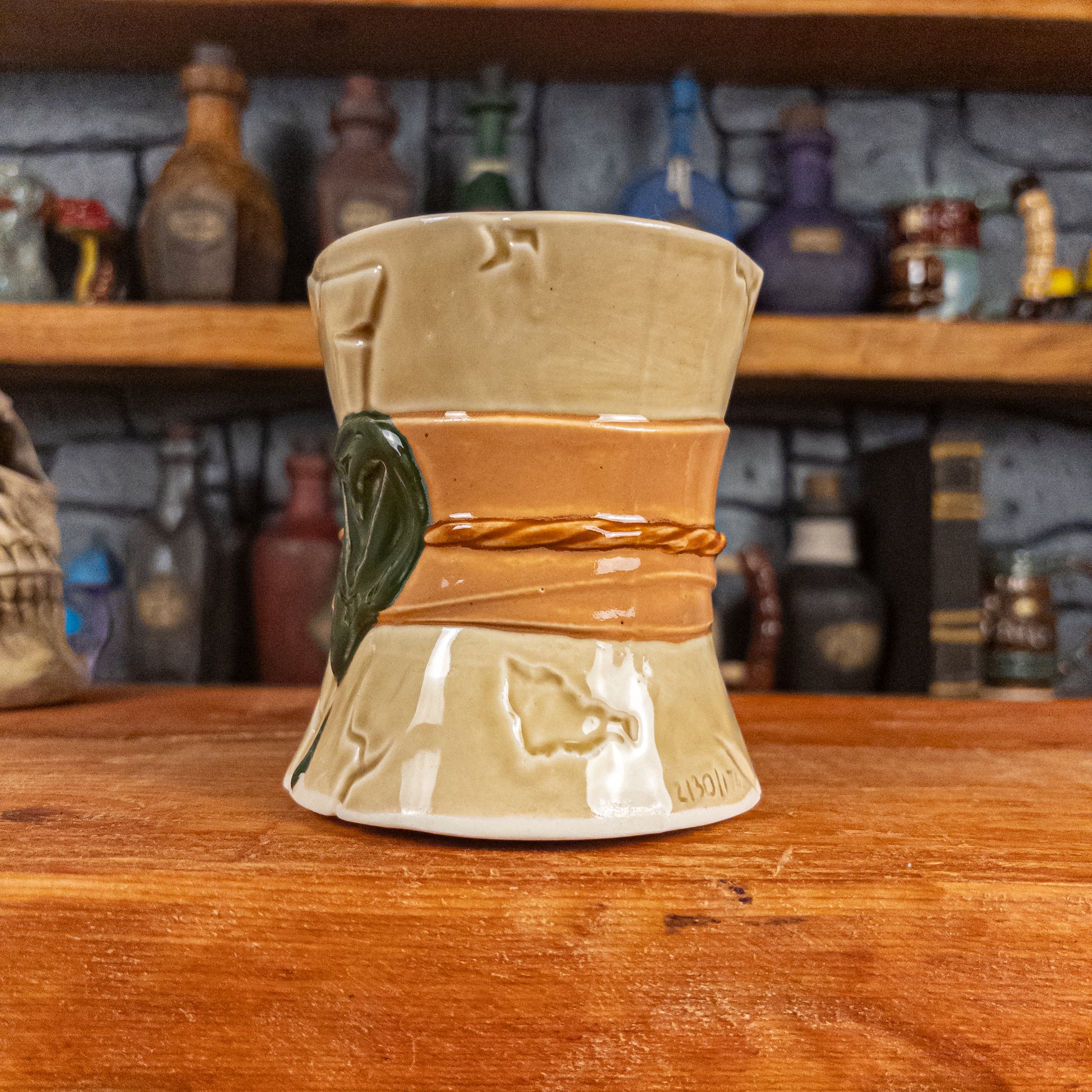 Three-quarter right side view of a handmade Scroll Mug designed to look like an old rolled parchment with a light yellow base, a light orange ribbon, a light brown cord and a dark green wax seal featuring a vampire emblem.