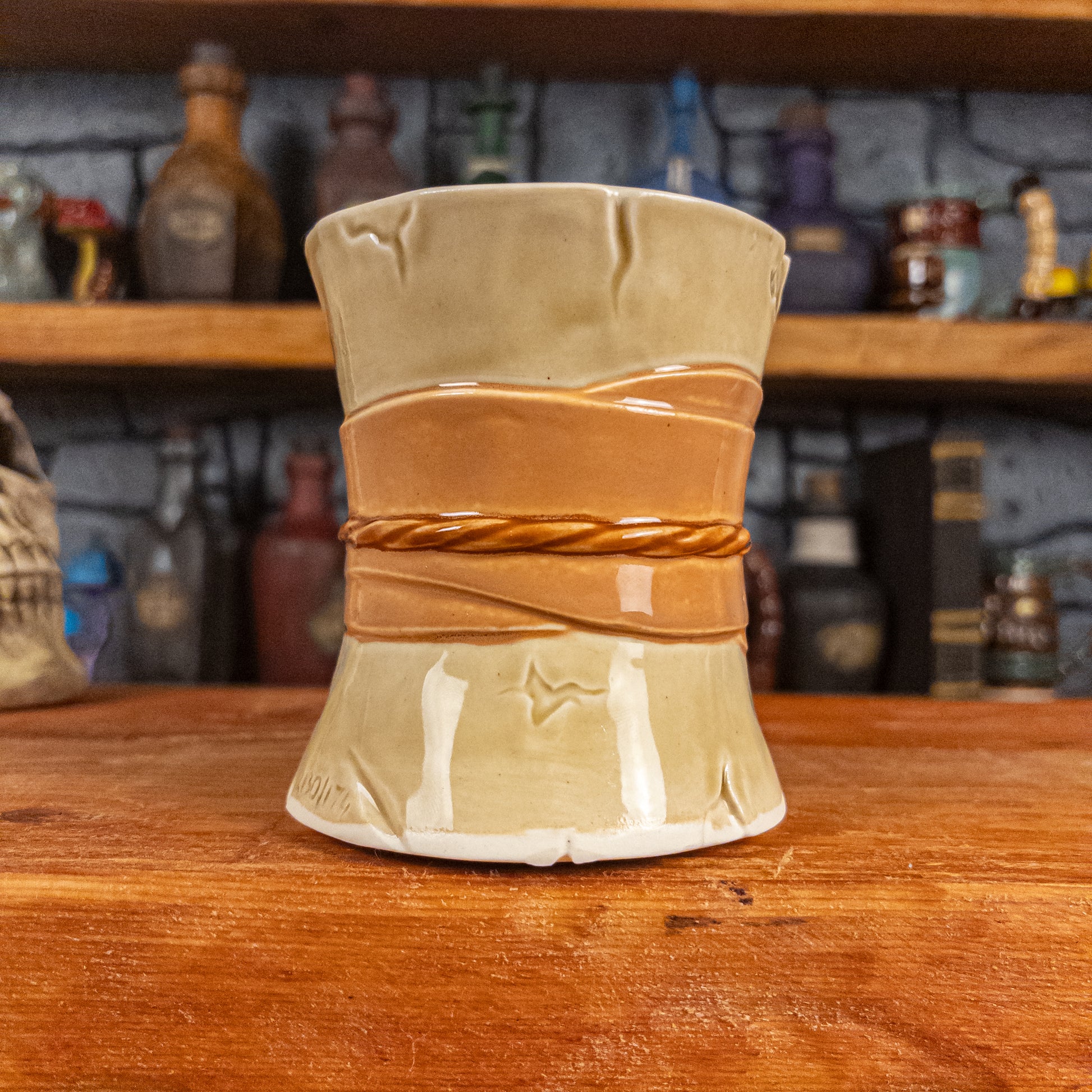 Back view of a handmade Scroll Mug designed to look like an old rolled parchment with a light-yellow base, a light orange ribbon and a light brown cord.