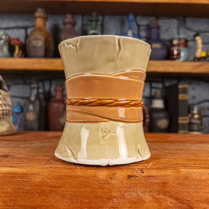 Back view of a handmade Scroll Mug designed to look like an old rolled parchment with a light-yellow base, a light orange ribbon and a light brown cord.