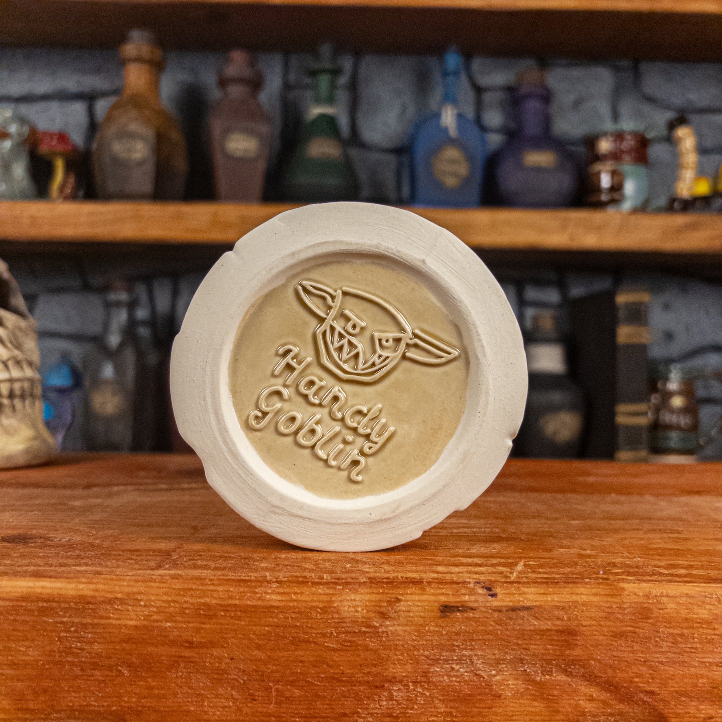 Bottom view of a handmade Scroll Mug with the Handy Goblin logo embossed in the centre, featuring a light-yellow base.