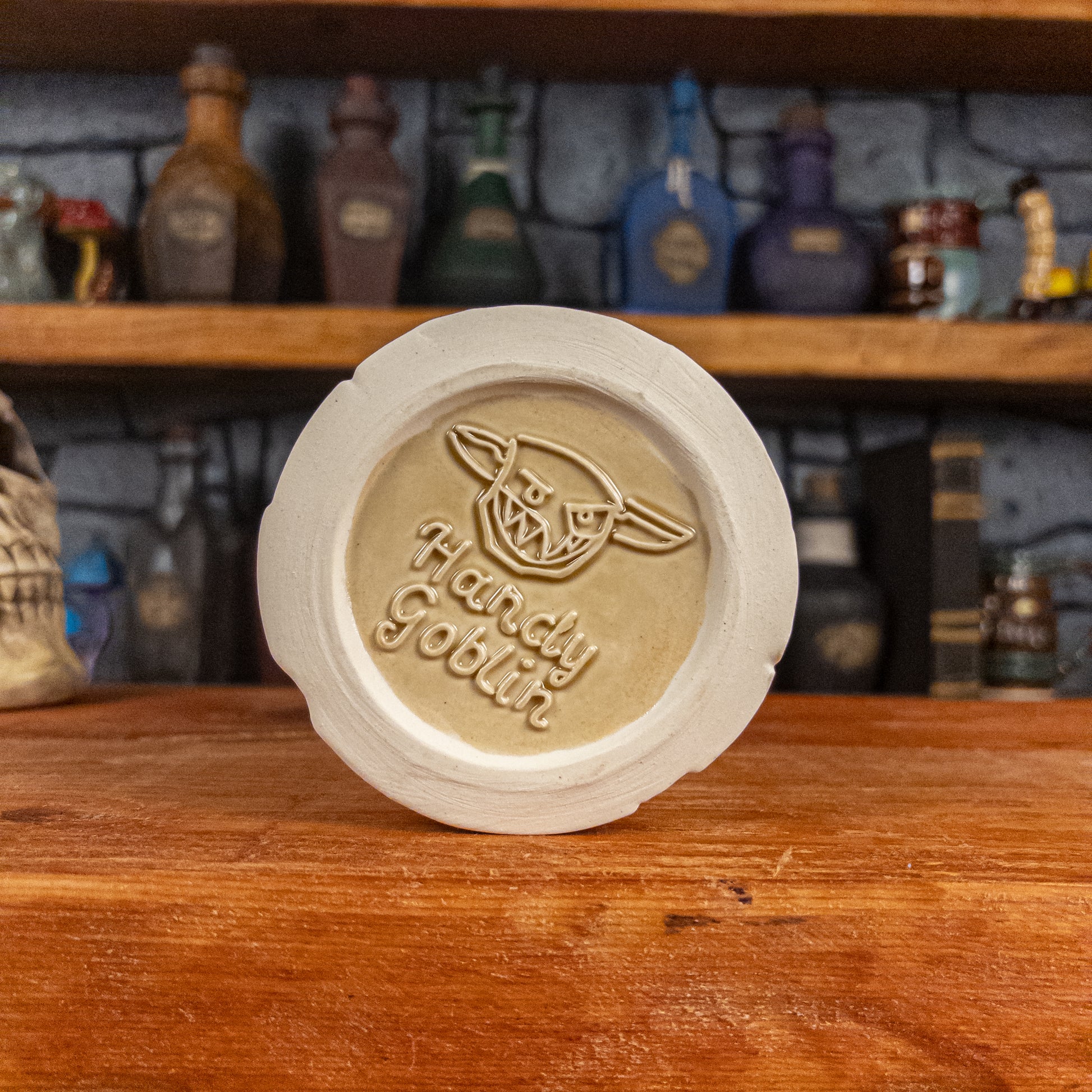 Bottom view of a handmade Scroll Mug with the Handy Goblin logo embossed in the centre, featuring a light-yellow base.