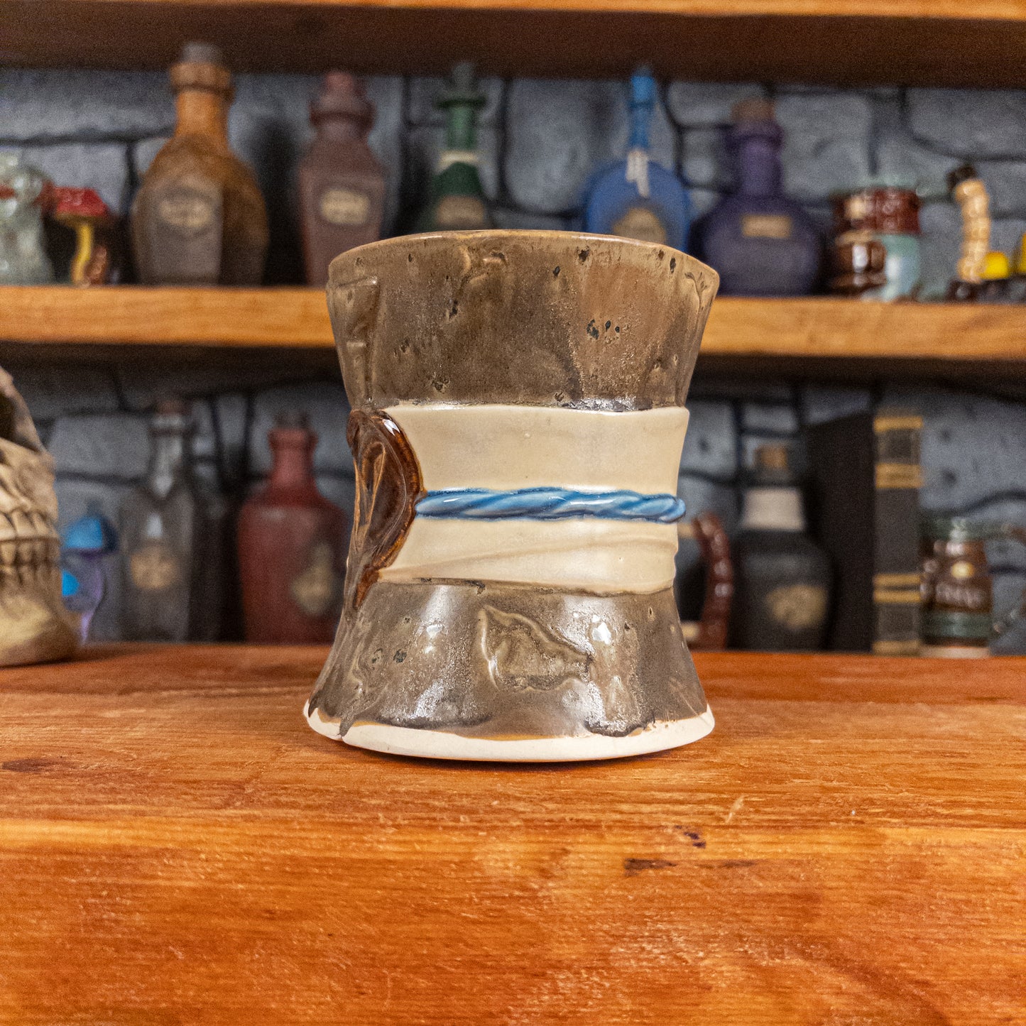 Three-quarter right side view of a handmade Scroll Mug designed to look like an old rolled parchment with a speckled dark brown base, an alabaster ribbon, a light blue cord and a reddish-brown wax seal featuring a vampire emblem.