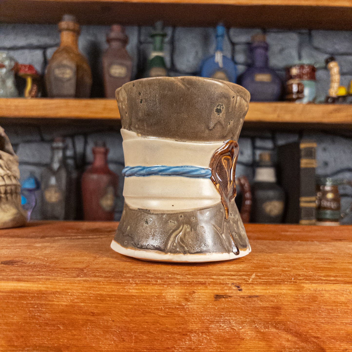 Three-quarter left side view of a handmade Scroll Mug designed to look like an old rolled parchment with a speckled dark brown base, an alabaster ribbon, a light blue cord and a reddish-brown wax seal featuring a vampire emblem.