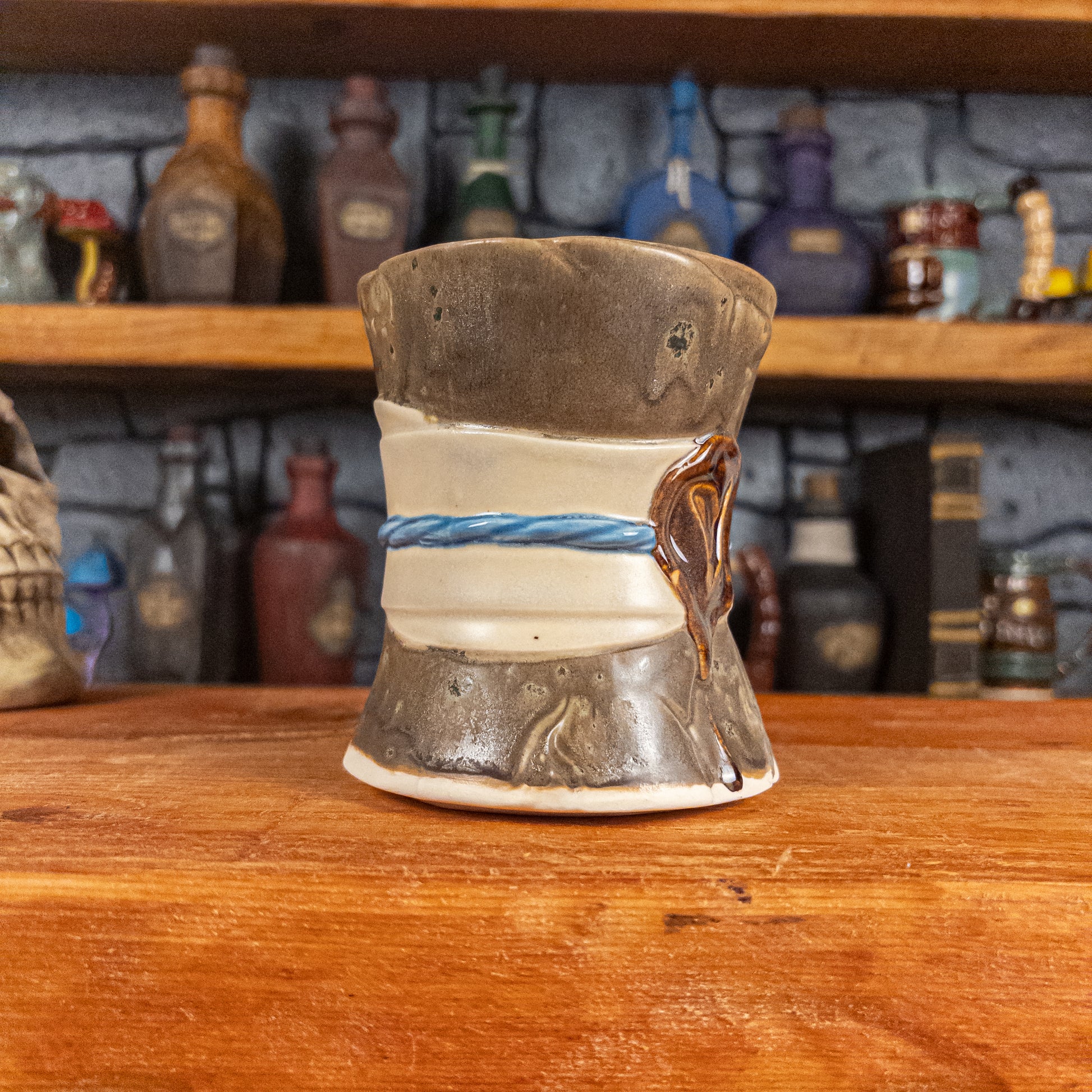Three-quarter left side view of a handmade Scroll Mug designed to look like an old rolled parchment with a speckled dark brown base, an alabaster ribbon, a light blue cord and a reddish-brown wax seal featuring a vampire emblem.