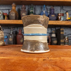 Back view of a handmade Scroll Mug designed to look like an old rolled parchment with a speckled dark brown base, an alabaster ribbon and a light blue cord.