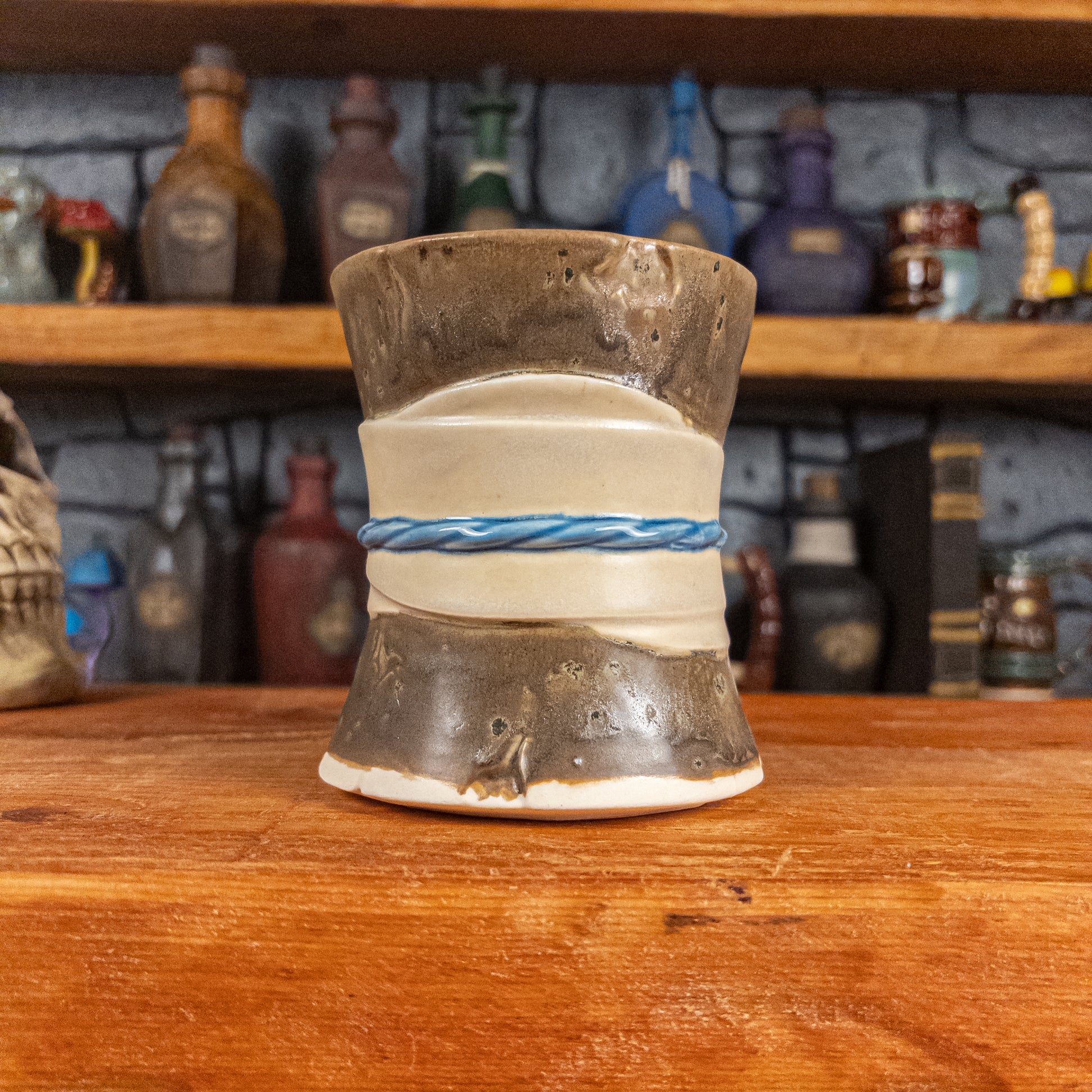 Back view of a handmade Scroll Mug designed to look like an old rolled parchment with a speckled dark brown base, an alabaster ribbon and a light blue cord.