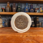 Bottom view of a handmade Scroll Mug with the Handy Goblin logo embossed in the centre, featuring a speckled dark brown base.