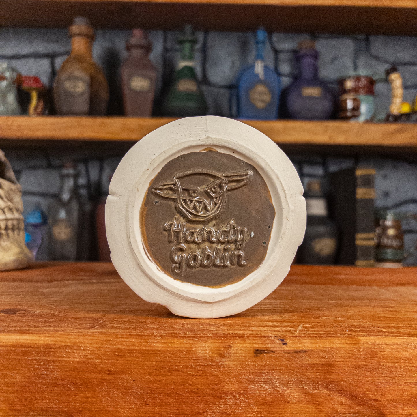 Bottom view of a handmade Scroll Mug with the Handy Goblin logo embossed in the centre, featuring a speckled dark brown base.