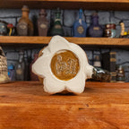 The bottom view of a handmade Coin Bag Mug with the Handy Goblin logo embossed in the centre, featuring a dark gold base with the visible bottom of the four fingers.