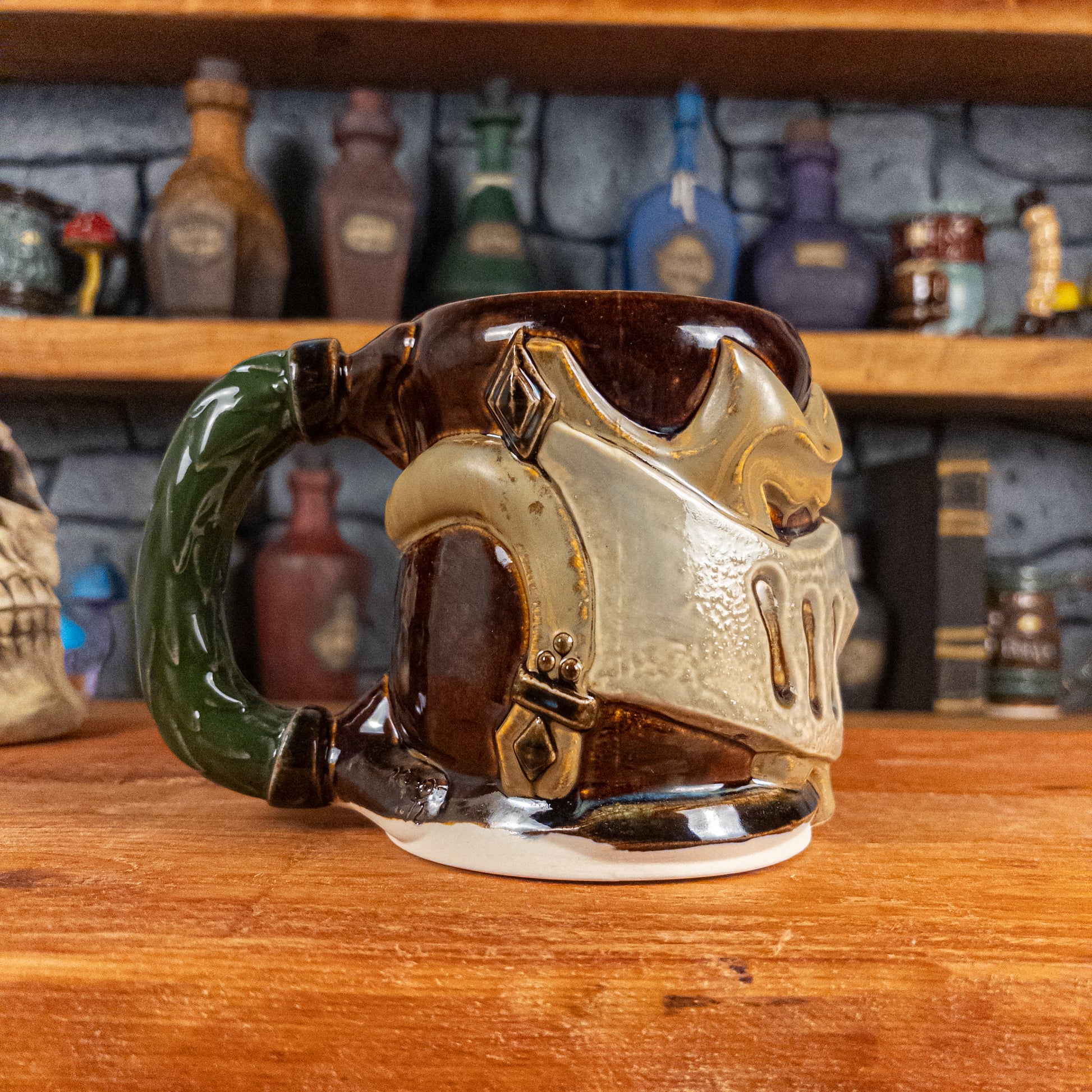 The left side view of a handmade Knight Helmet Mug with a brown, beige, and grey armour design, featuring ornamental rivets and a detailed green handle.