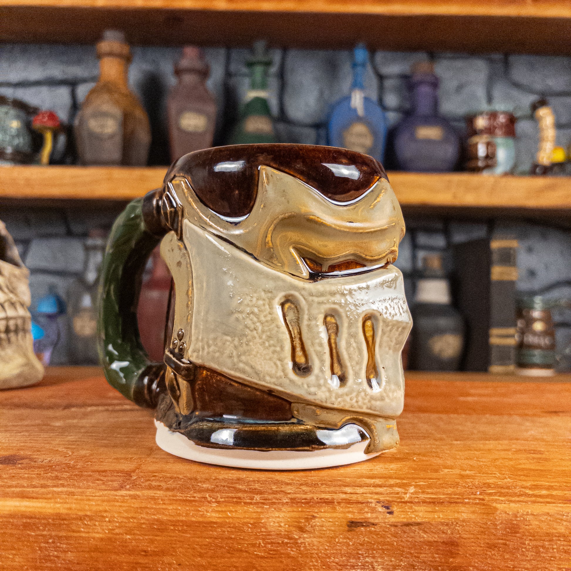 Three-quarter left side view of a handmade Knight Helmet Mug with a brown, beige and grey armour design, featuring ornamental rivets and a detailed green handle.
