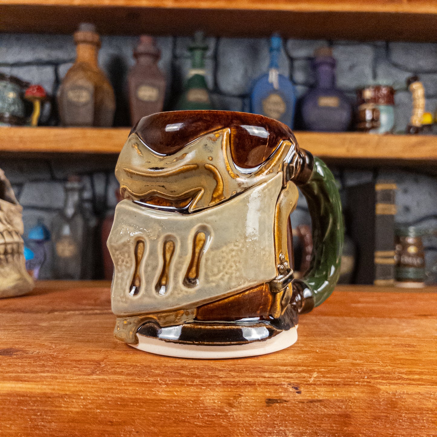Three-quarter right side view of a handmade Knight Helmet Mug with a brown, beige and grey armour design, featuring ornamental rivets and a detailed green handle.