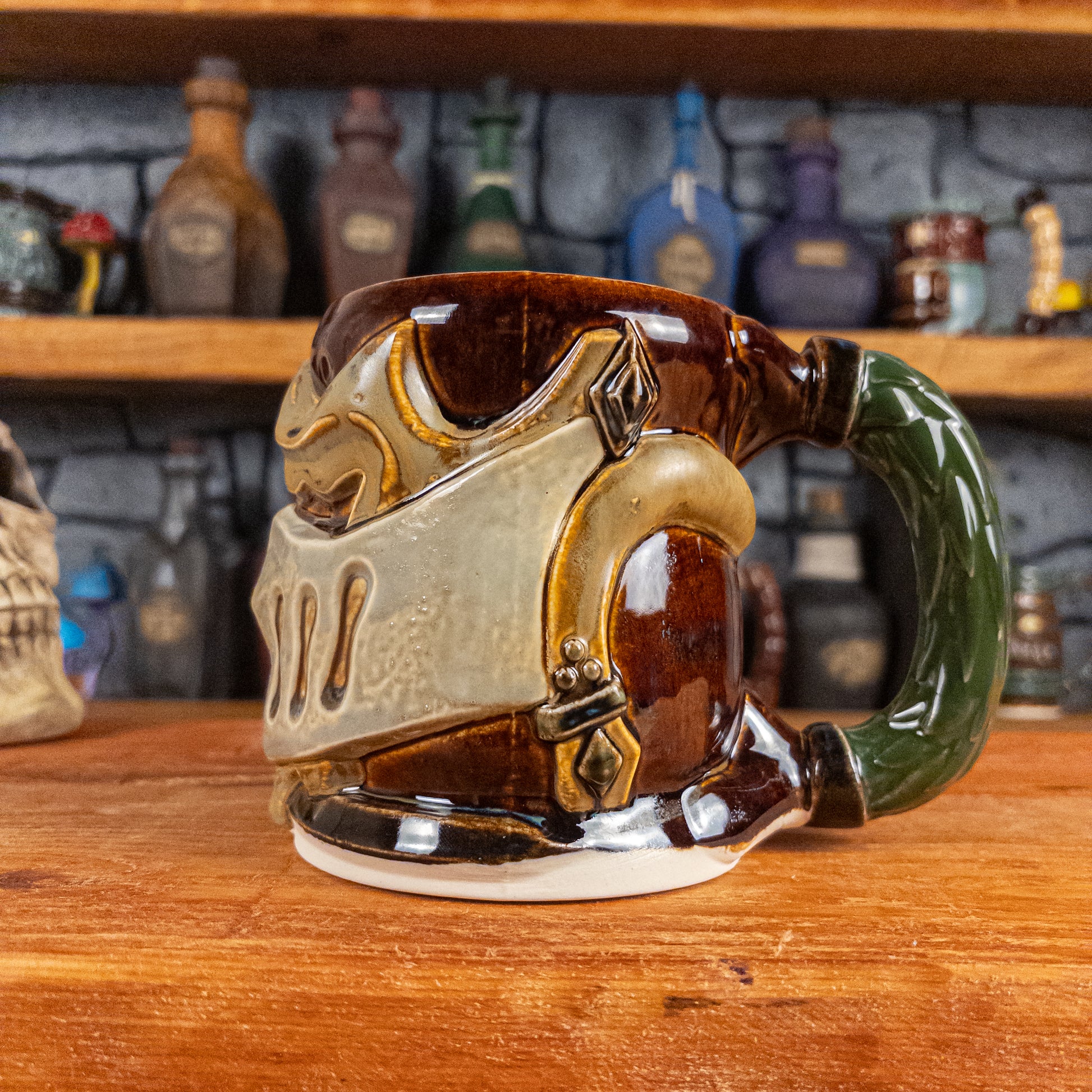 The right side view of a handmade Knight Helmet Mug with a brown, beige, and grey armour design, featuring ornamental rivets and a detailed green handle.