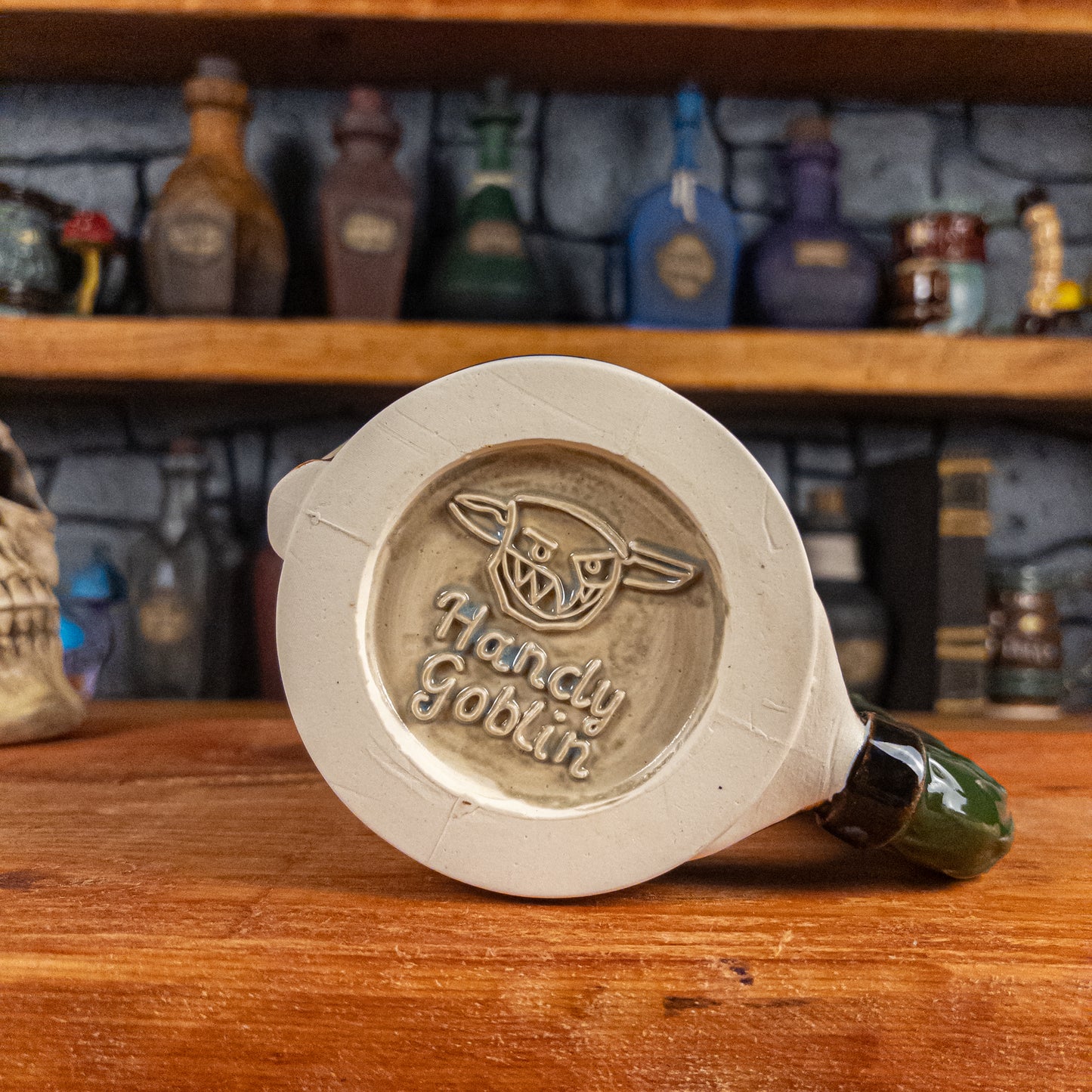 Bottom view of a handmade Knight Helmet Mug with the Handy Goblin logo embossed in the centre, featuring a grey base.