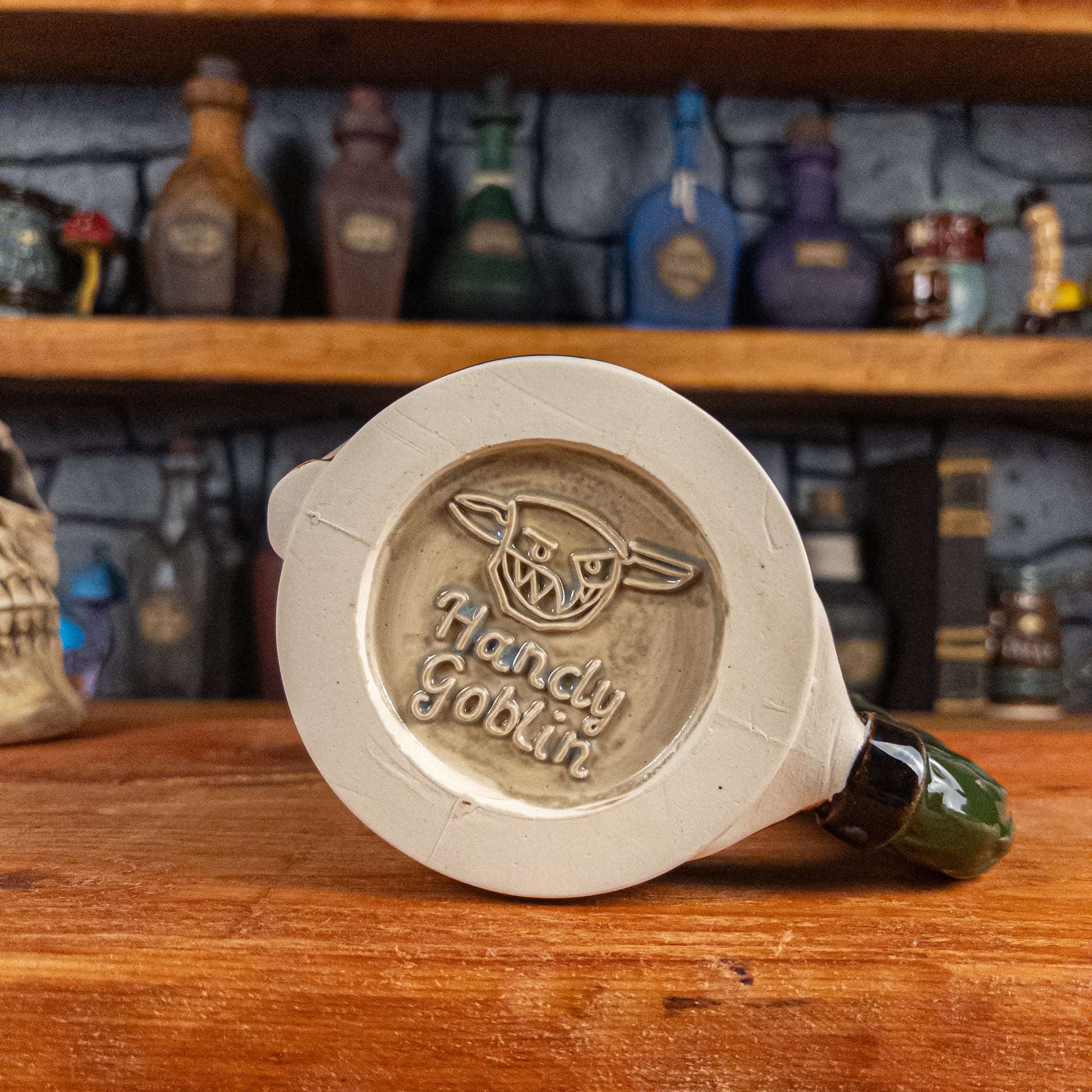 Bottom view of a handmade Knight Helmet Mug with the Handy Goblin logo embossed in the centre, featuring a grey base.