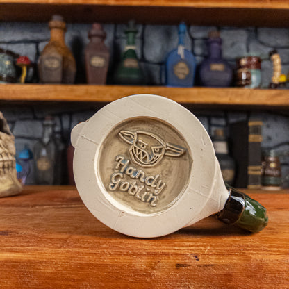 Bottom view of a handmade Knight Helmet Mug with the Handy Goblin logo embossed in the centre, featuring a grey base.