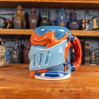 Three-quarter right side view of a handmade Knight Helmet Mug with a light blue, blue and red-orange armour design, featuring dark blue ornamental rivets and a detailed red handle.